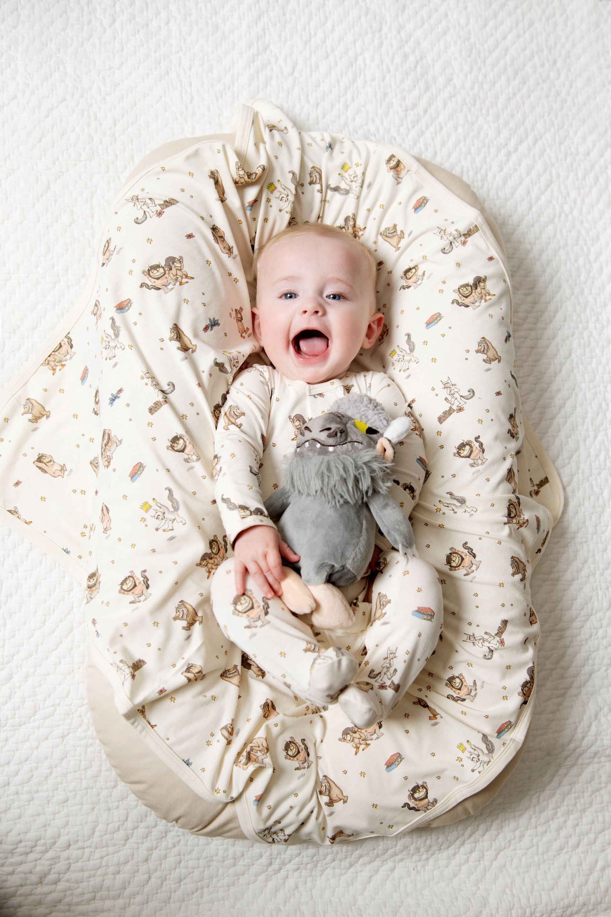 Baby sitting in a Where the Wild Things are nest holding a plush toy on a white background