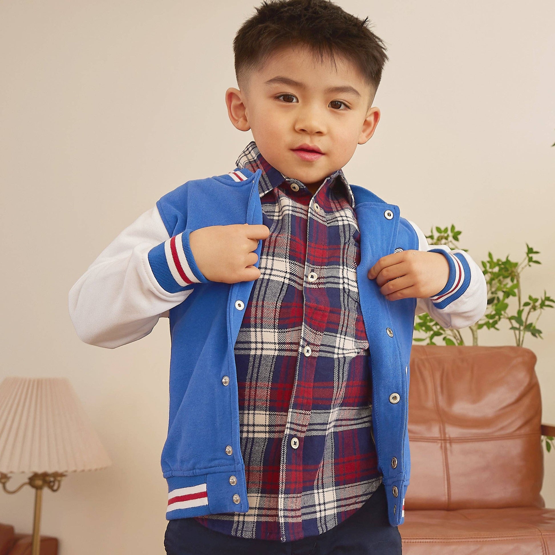 Boy wearing a blue bomber jacket in a room with white walls.