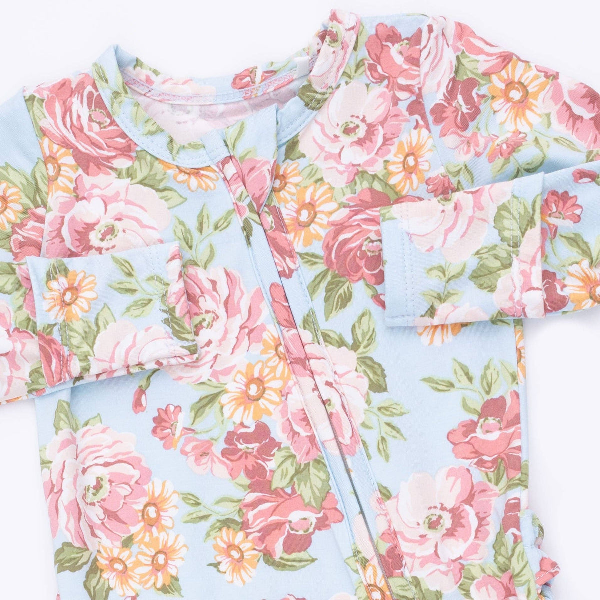 A close-up of a baby romper or long-sleeve top with a light blue background and a vibrant floral print featuring pink, red, and orange flowers with green leaves.
