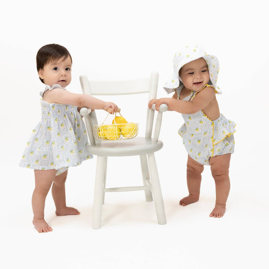Two young children in matching outfits with a white chair and yellow basket on a white background