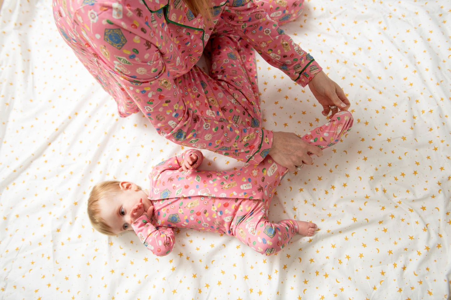 mom and baby in matching pink pajamas on a white bed with yellow dots.