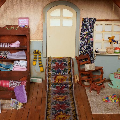 Dollhouse interior with furniture, decorations, and a colorful rug.