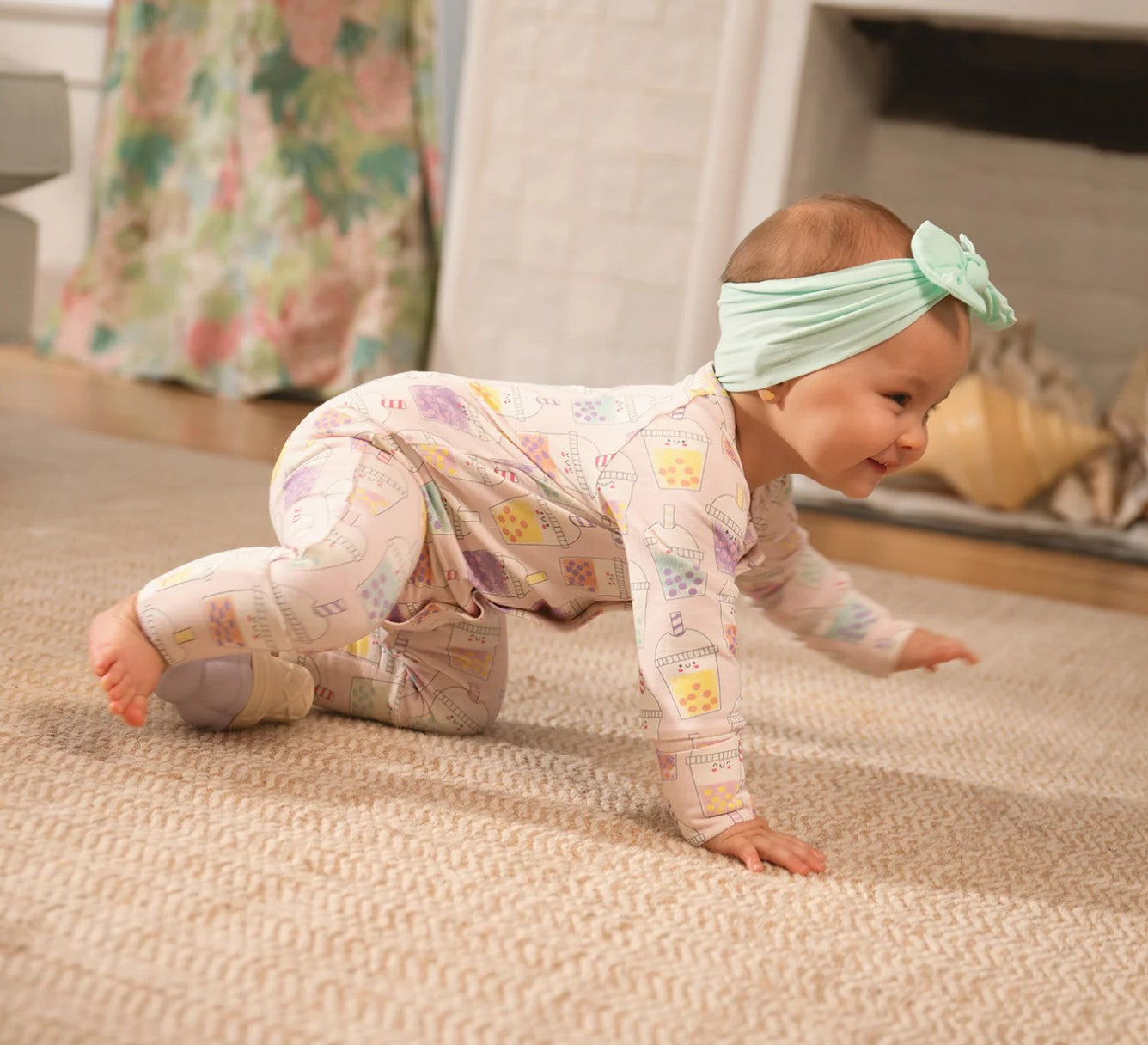 Baby in a patterned onesie and headband crawling on a carpeted floor.