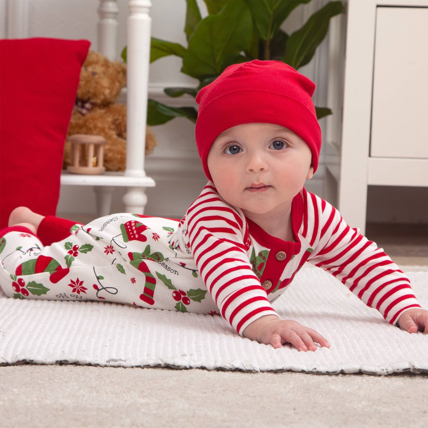 Baby in holiday outfit lying on a rug with a teddy bear in the background