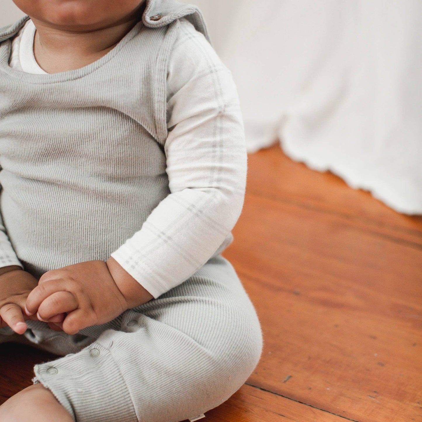close up of Baby in a light gray outfit sitting on a wooden floor