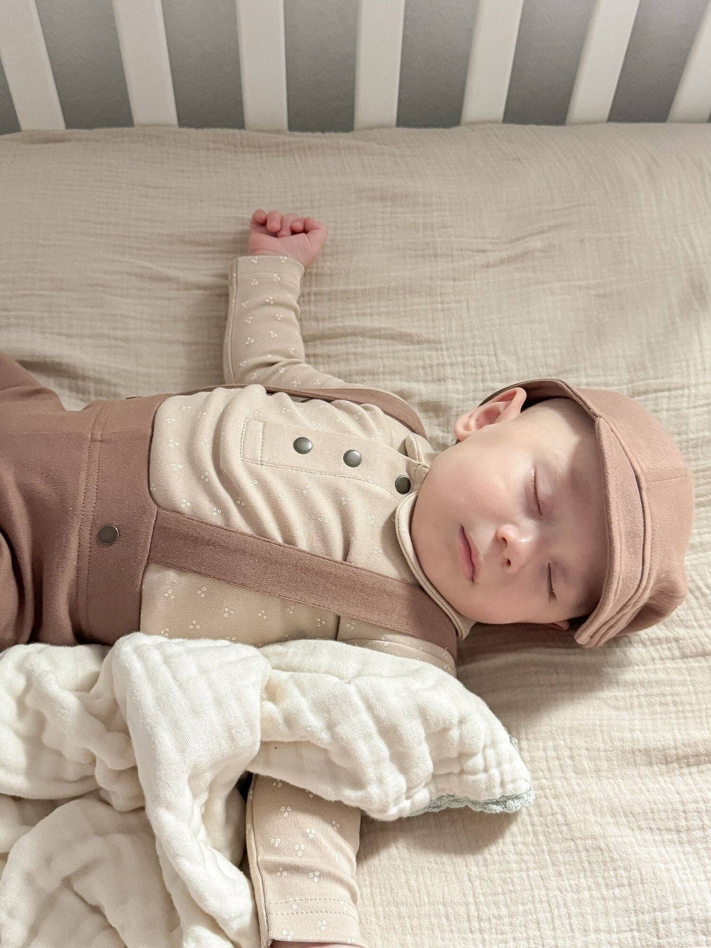 Baby sleeping in a crib with a brown hat and pants with beige shirt