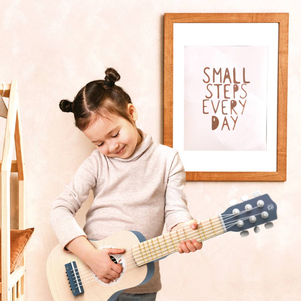Child playing a toy guitar with a framed quote on the wall