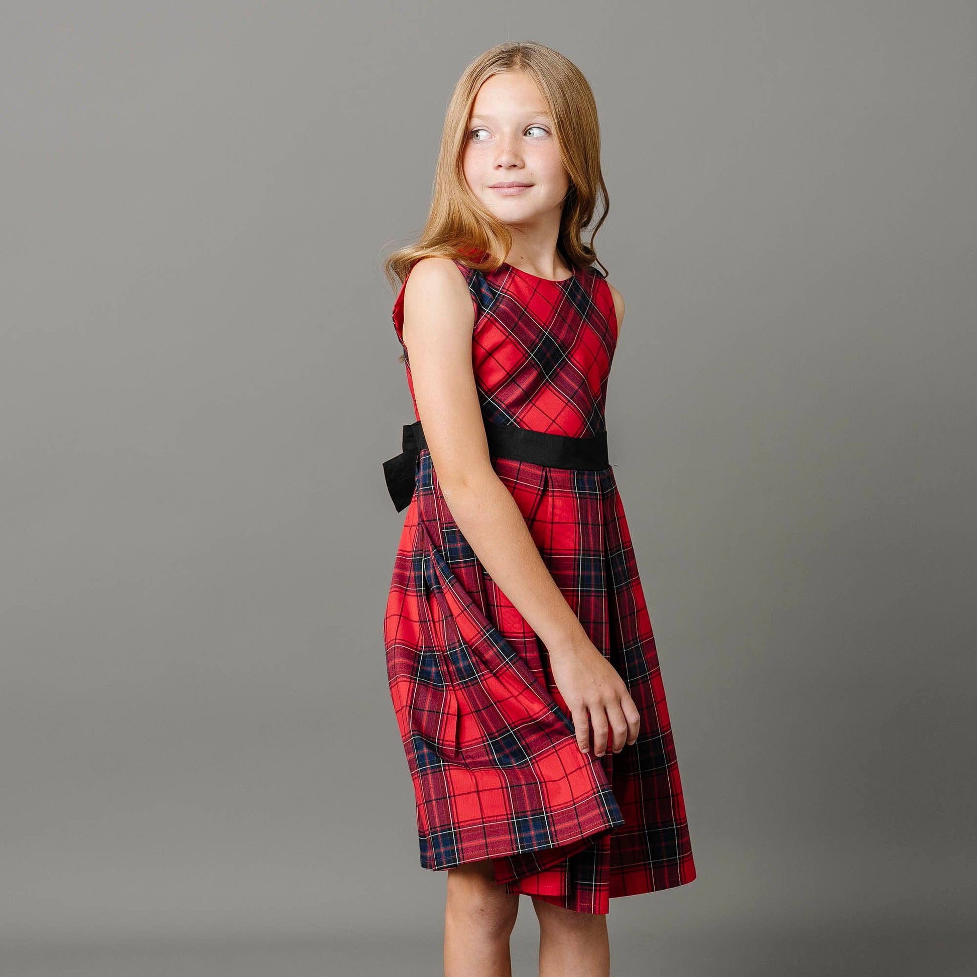 Young girl wearing a red plaid dress against a gray background