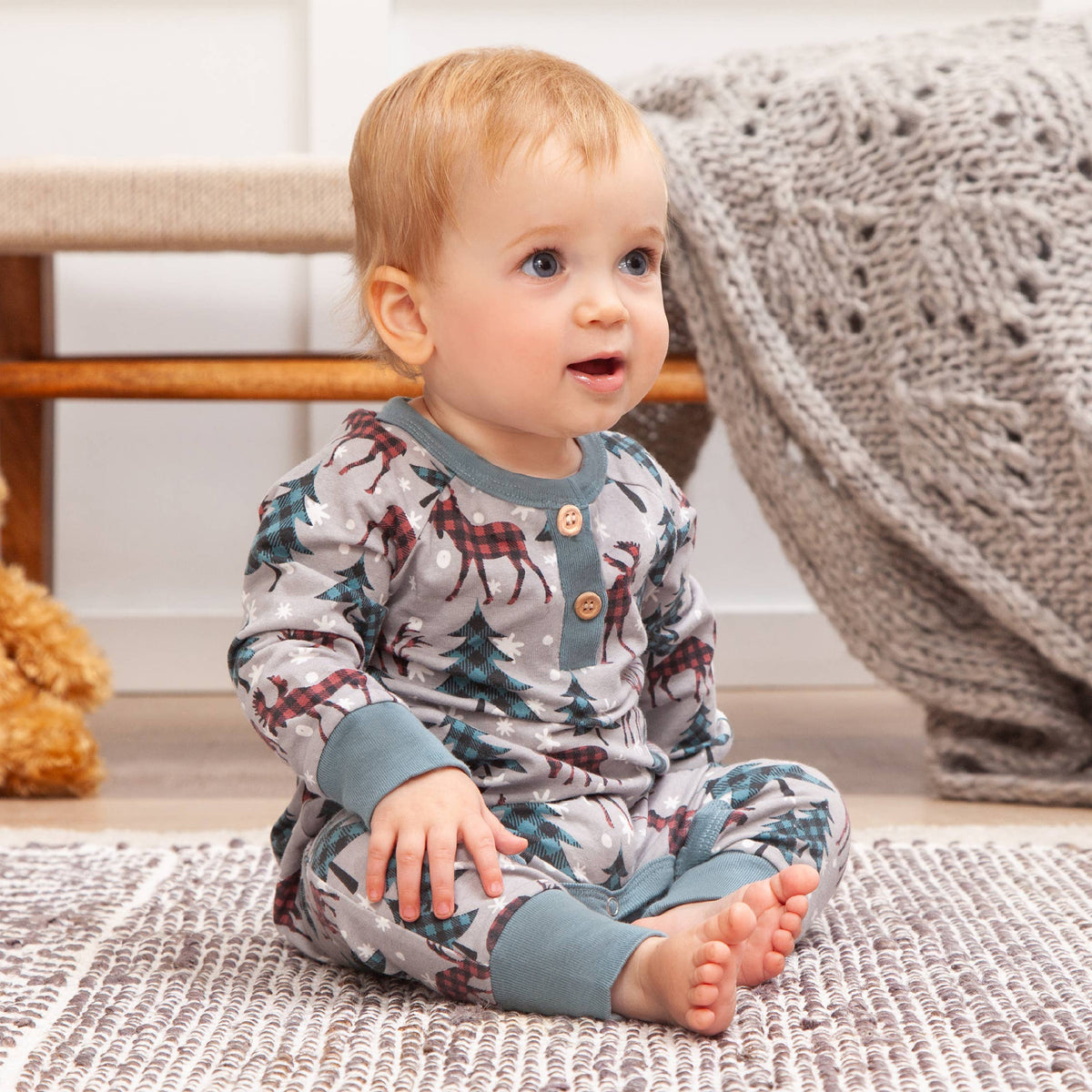Baby wearing a patterned onesie sitting on a rug.