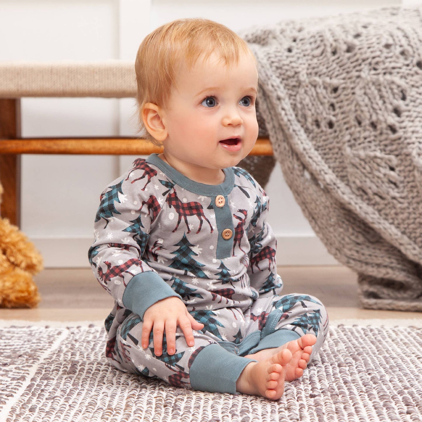 Baby wearing a patterned onesie sitting on a rug.