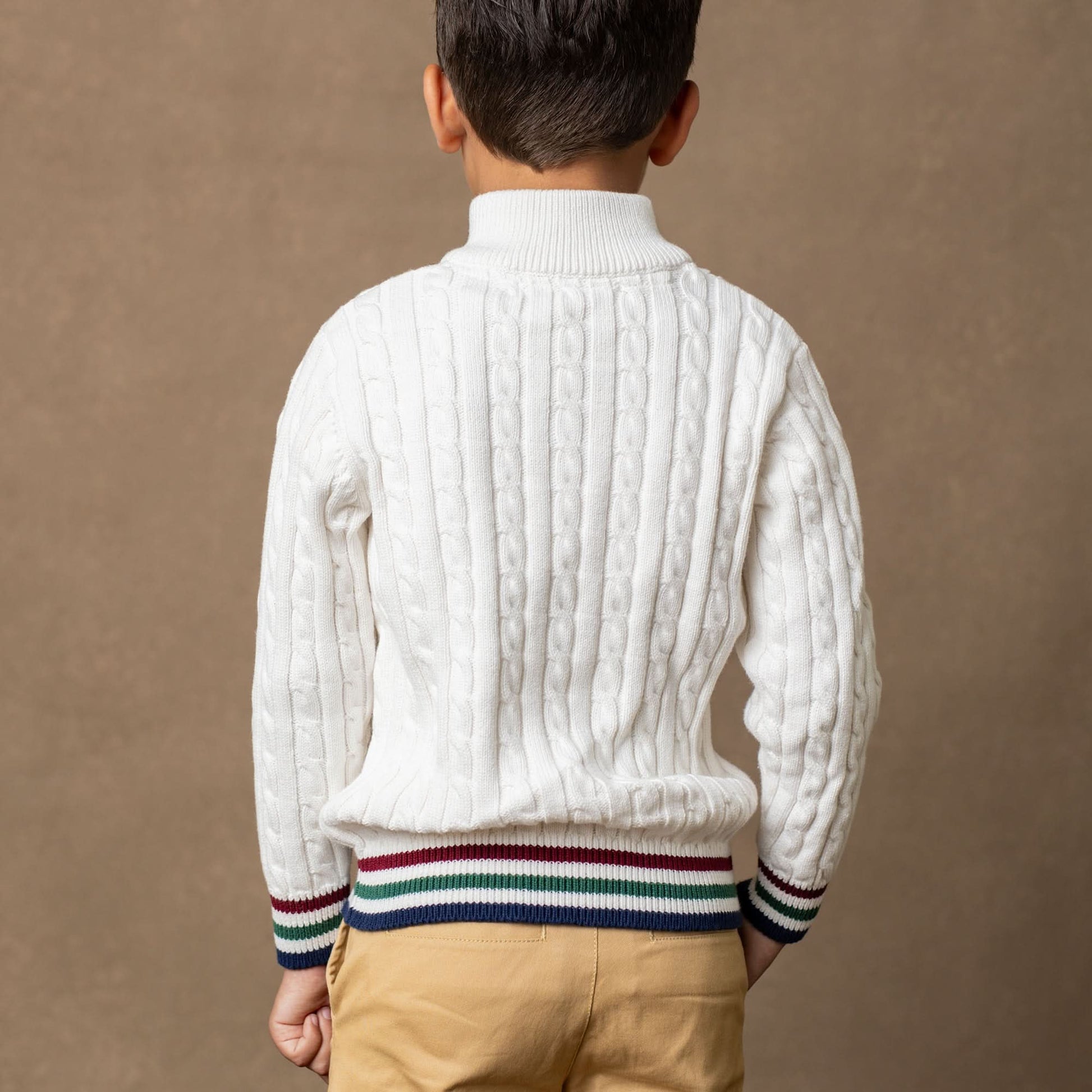 Person wearing a white cable knit sweater with colorful stripes on a brown background