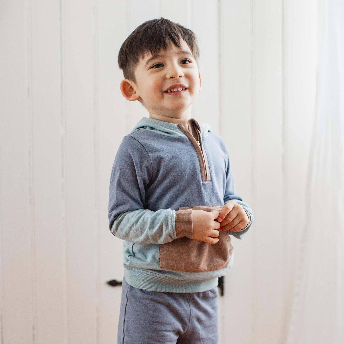 Child wearing a light blue sweater with a pink pocket against a white wall