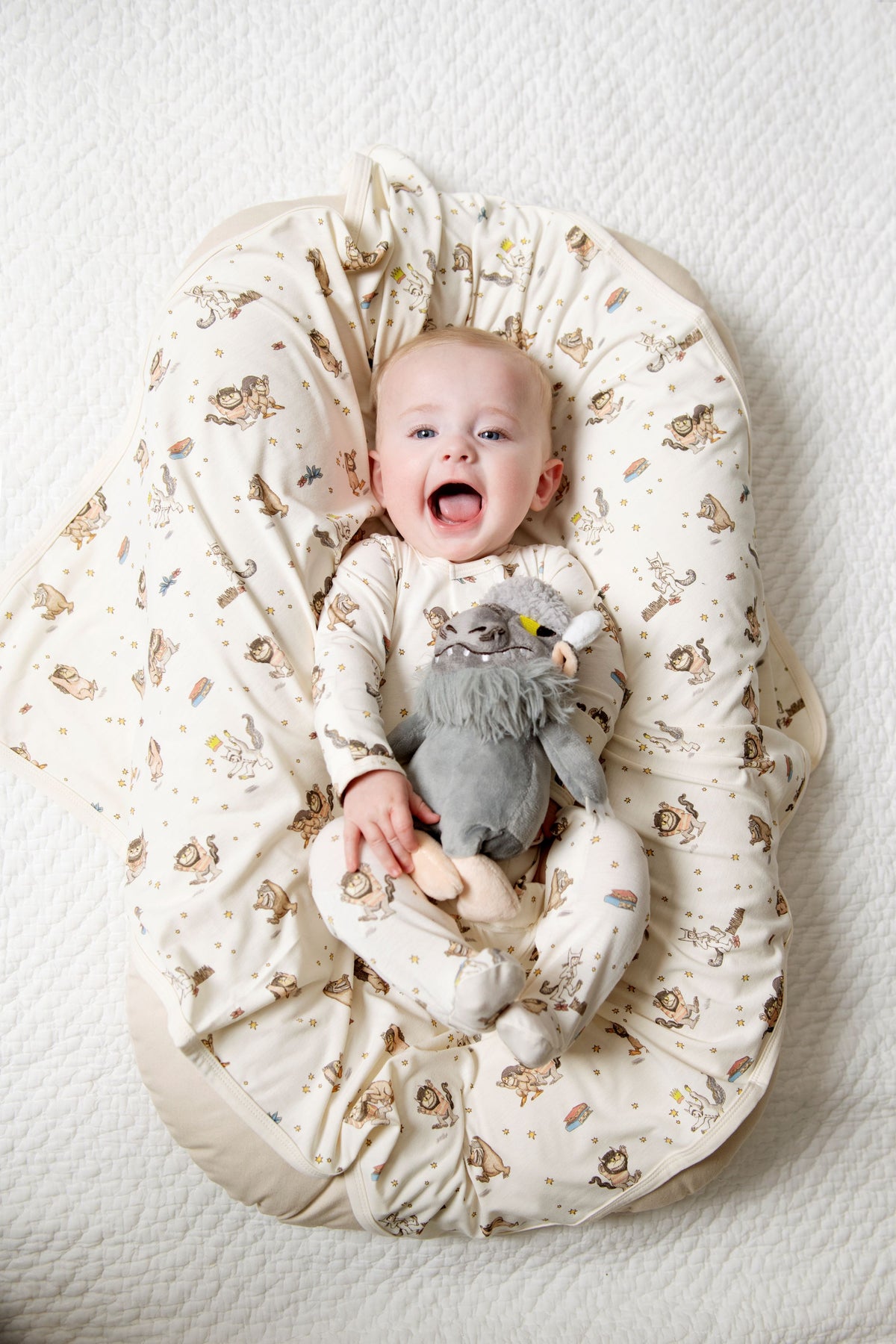 Baby sitting in a Where the Wild Things are nest holding a plush toy on a white background