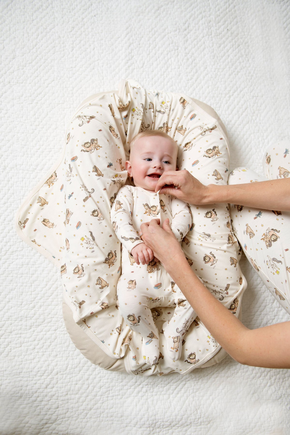 Baby wrapped in a Where the Wild Things are romper with a person's hand fastening the magnet closure on a background
