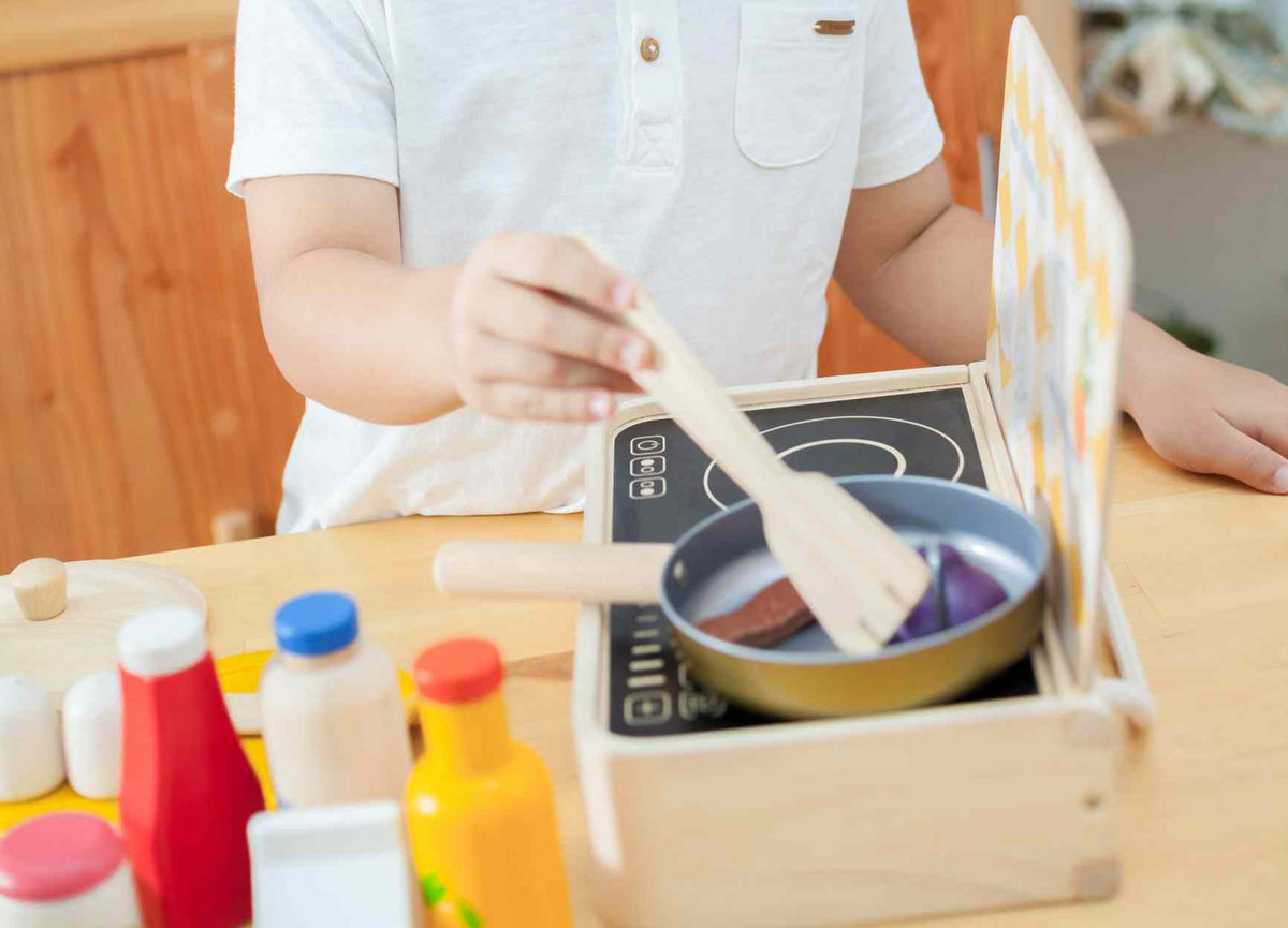 Child playing with a toy kitchen set on a wooden table