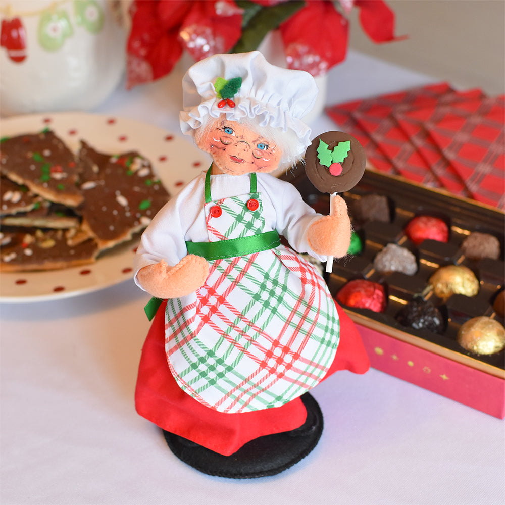 Annalee 9 inch Christmas Candy Mrs. Santa doll in a holly Santa hat and red, white and green plaid apron, holding a chocolate pop