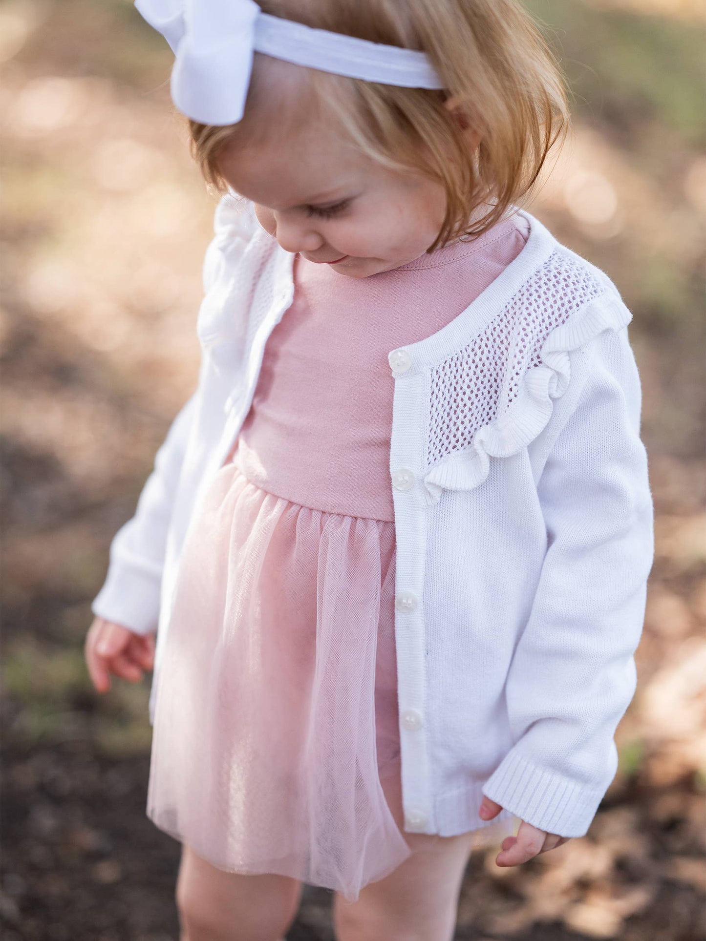 Child wearing a pink dress with a white cardigan in an outdoor setting