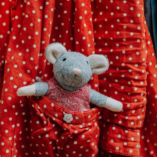 Stuffed mouse toy in red polka dot outfit against a red polka dot background