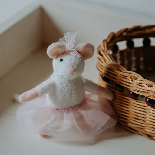 Stuffed mouse toy in a tutu dress next to a wicker basket on a light surface.