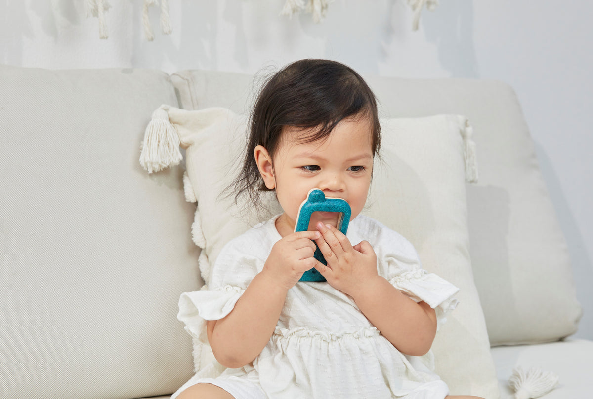 Child holding a blue phone toy on a white couch