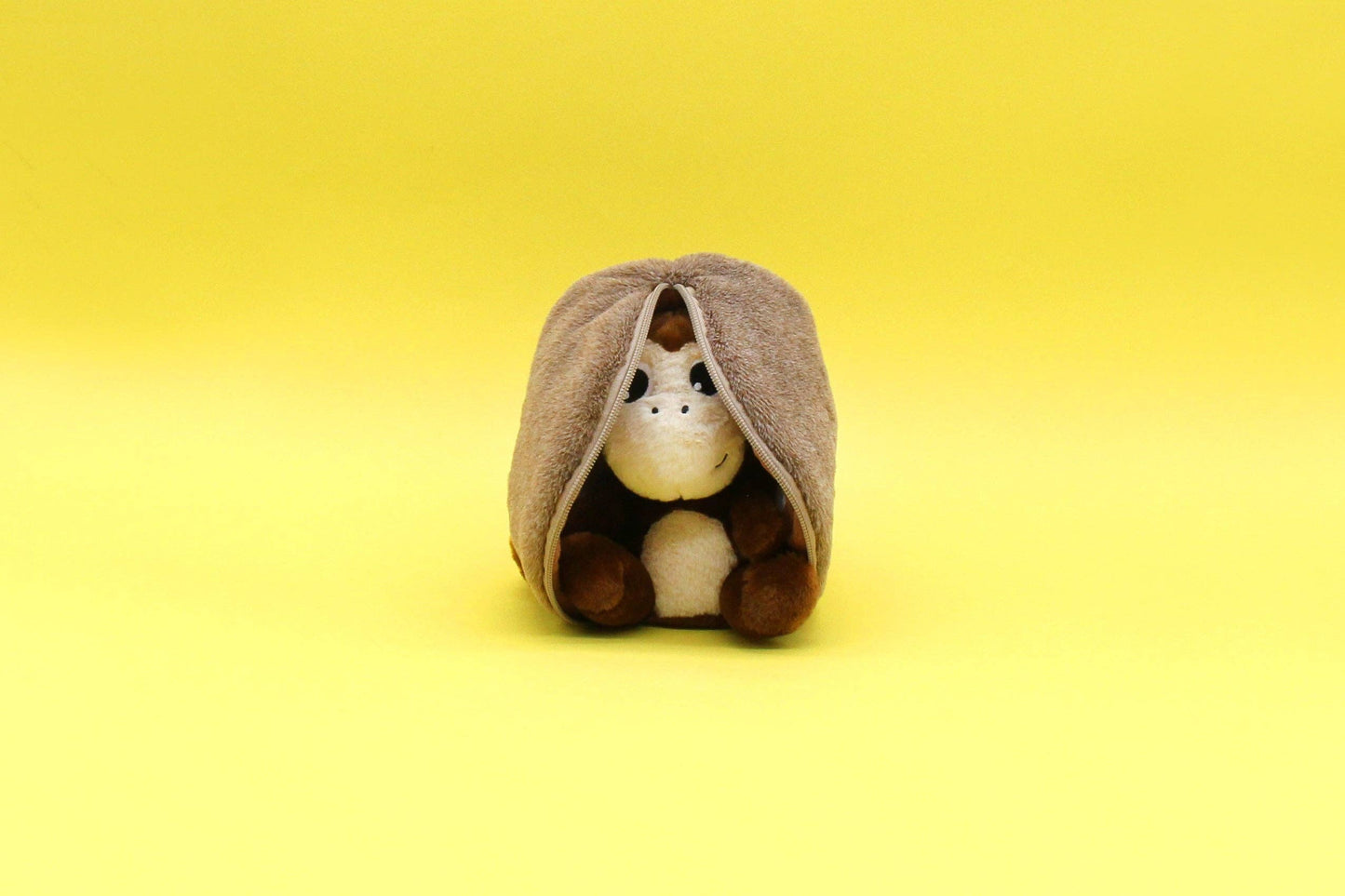 Small plush toy horse peeking out from a plush coconut on a yellow background