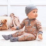 Baby wearing a brown onesie with animal patterns and gray hat and socks, sitting on a white floor.