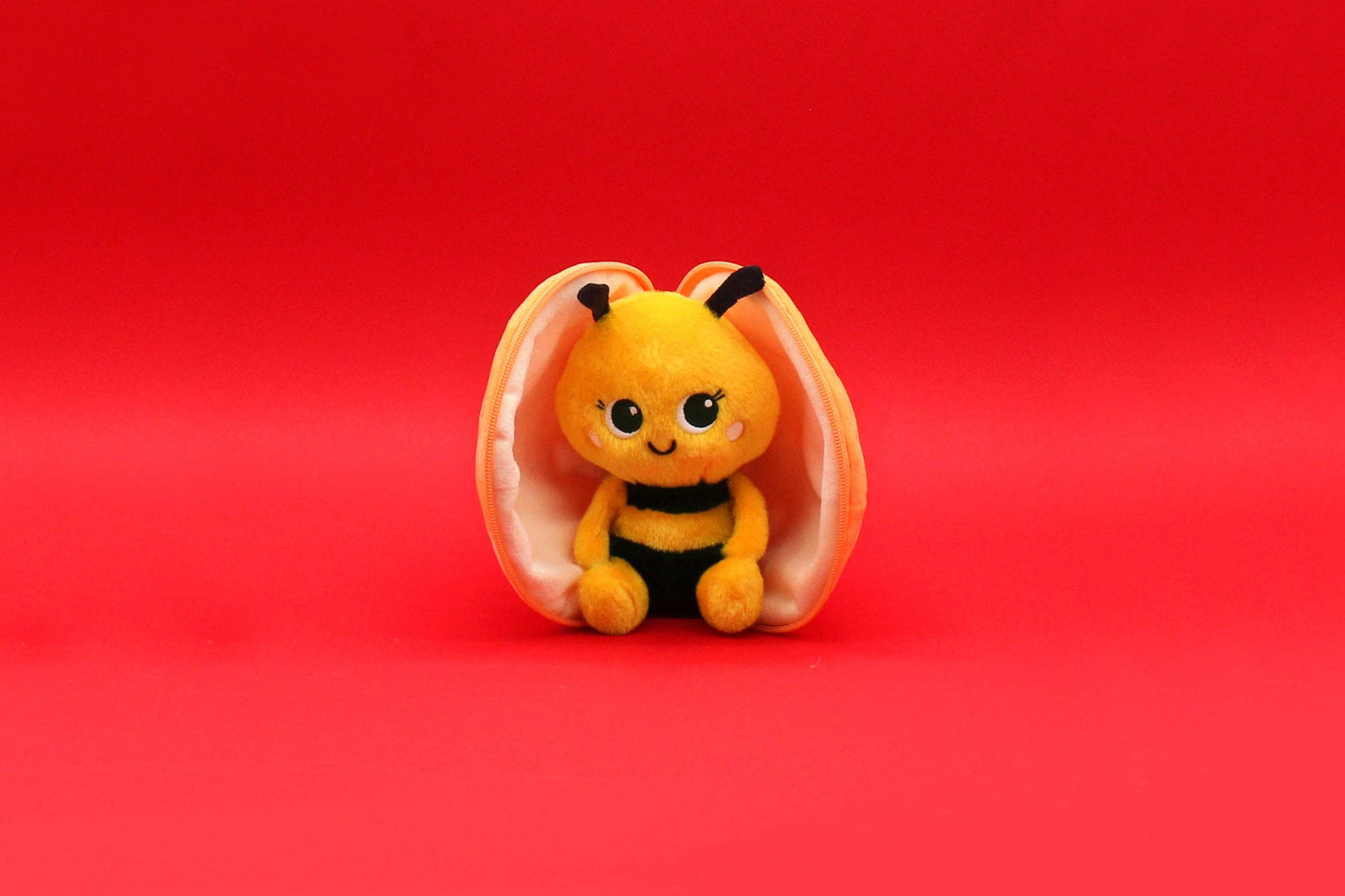Small plush bee toy inside a shell on a red background