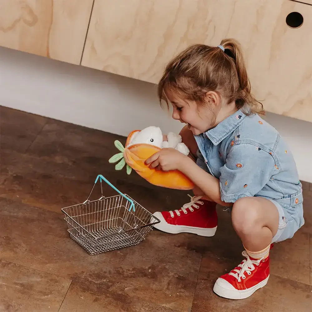 Child playing with a toy fruit and basket on a wooden floor.