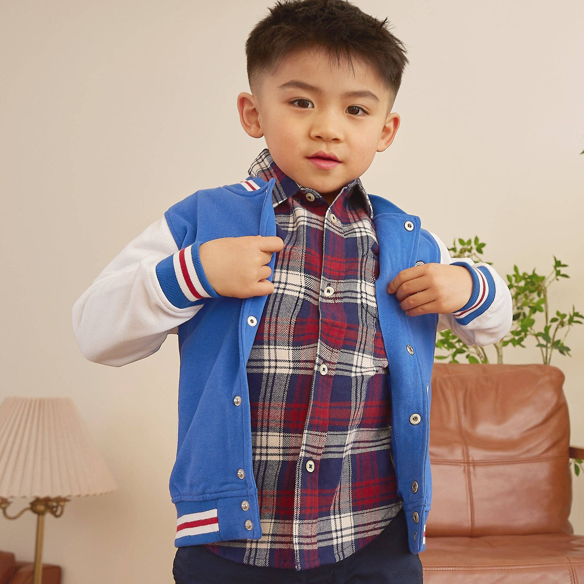 Boy wearing a light blue varsity jacket in a room with white walls