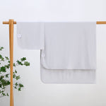 Light gray swaddle blankets hanging on a wooden rack against a white background with a plant on the left.