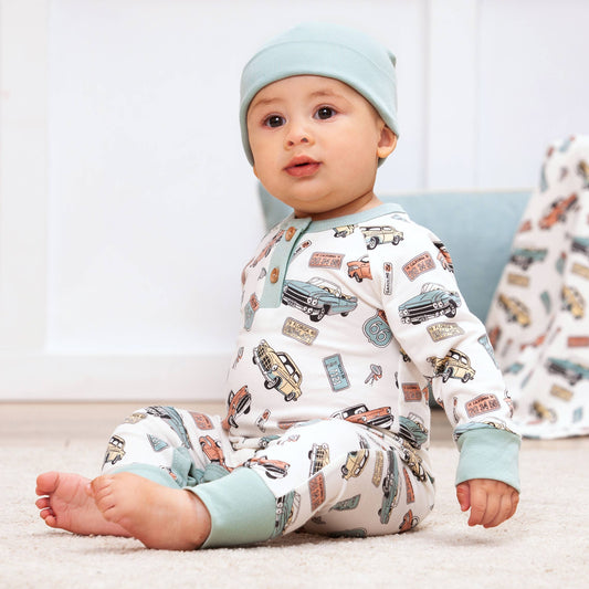 A baby wearing a Henley romper with a vintage cars print, paired with a matching hat.