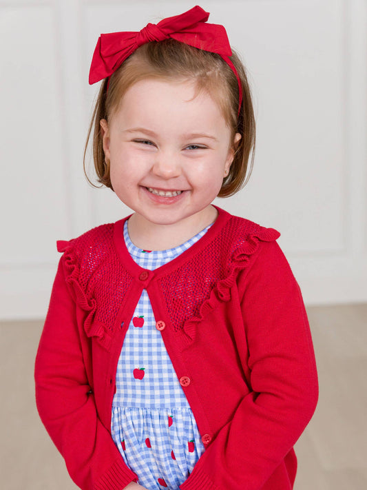 Child wearing a red sweater with ruffles and a matching headband, standing against a plain background.