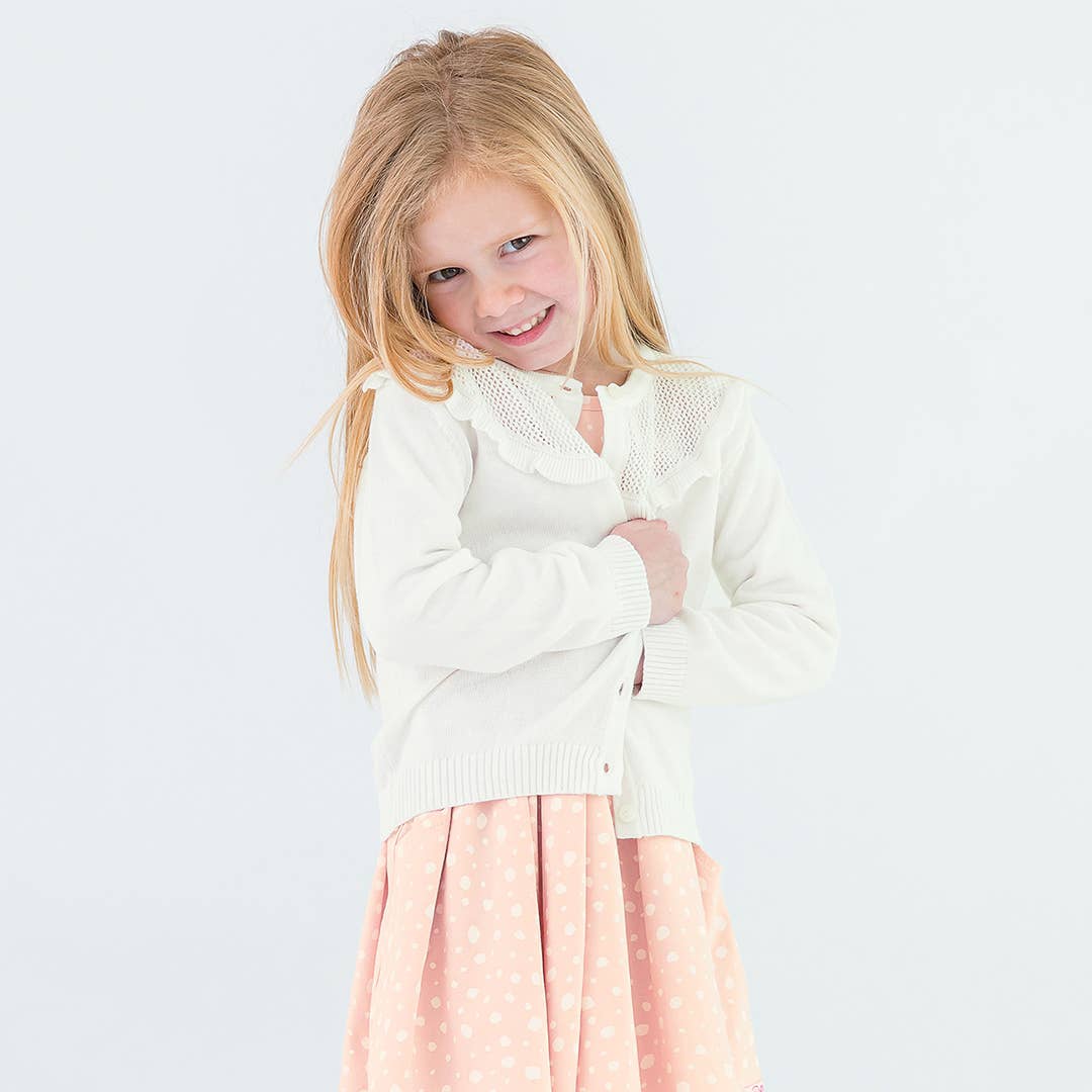 Young girl wearing a white sweater and pink skirt on a light gray background