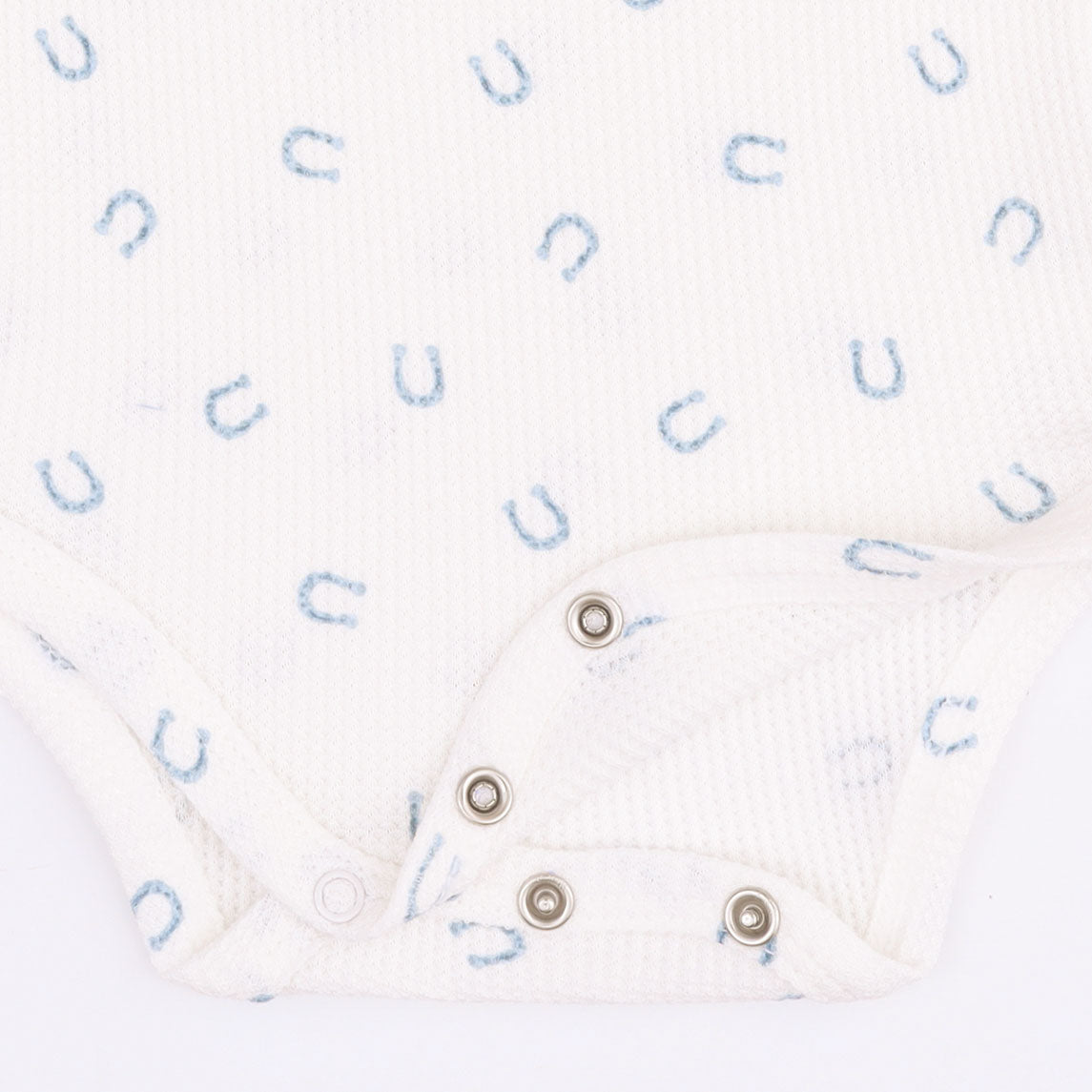 Close-up of a white ribbed baby bodysuit with a light blue horseshoe pattern and silver snap closures.