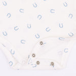 Close-up of a white ribbed baby bodysuit with a light blue horseshoe pattern and silver snap closures.