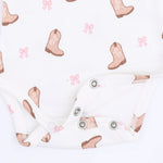 White ribbed baby bodysuit with a cowboy boot and pink bow pattern, featuring snap closures at the crotch.