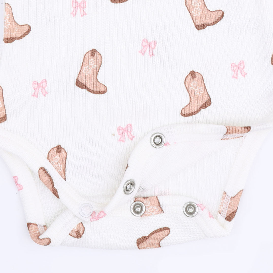 White ribbed baby bodysuit with a cowboy boot and pink bow pattern, featuring snap closures at the crotch.