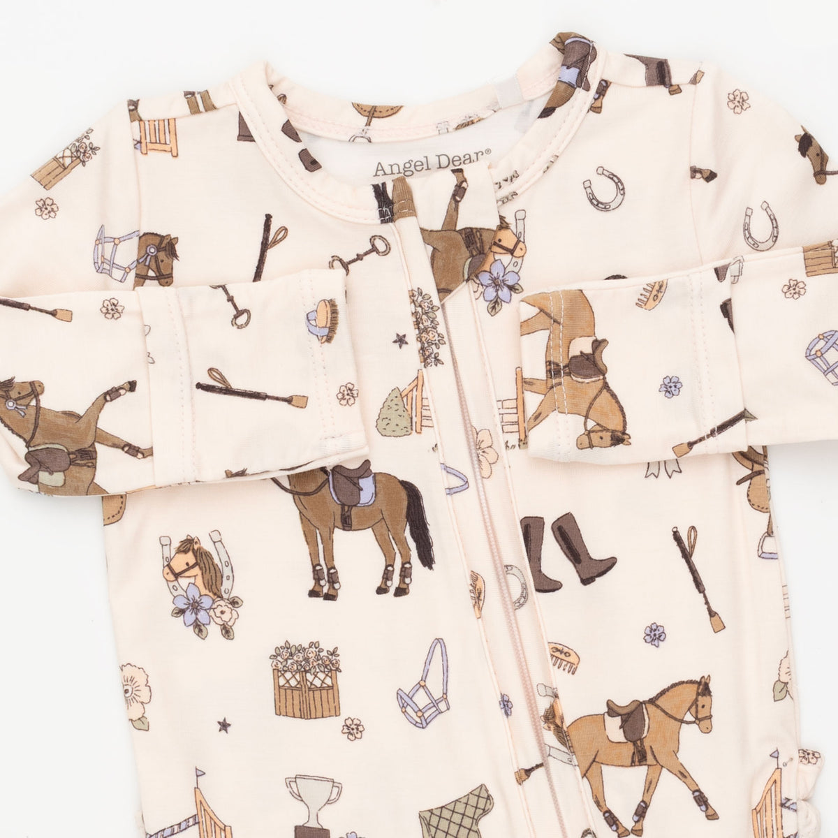 A long-sleeve baby zip-up footed sleeper by Angel Dean, featuring an all-over equestrian-themed print on a light cream background. The print includes brown horses, riders, horseshoes, riding boots, and tack.