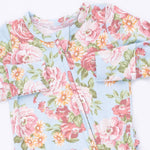 A close-up of a baby romper or long-sleeve top with a light blue background and a vibrant floral print featuring pink, red, and orange flowers with green leaves.