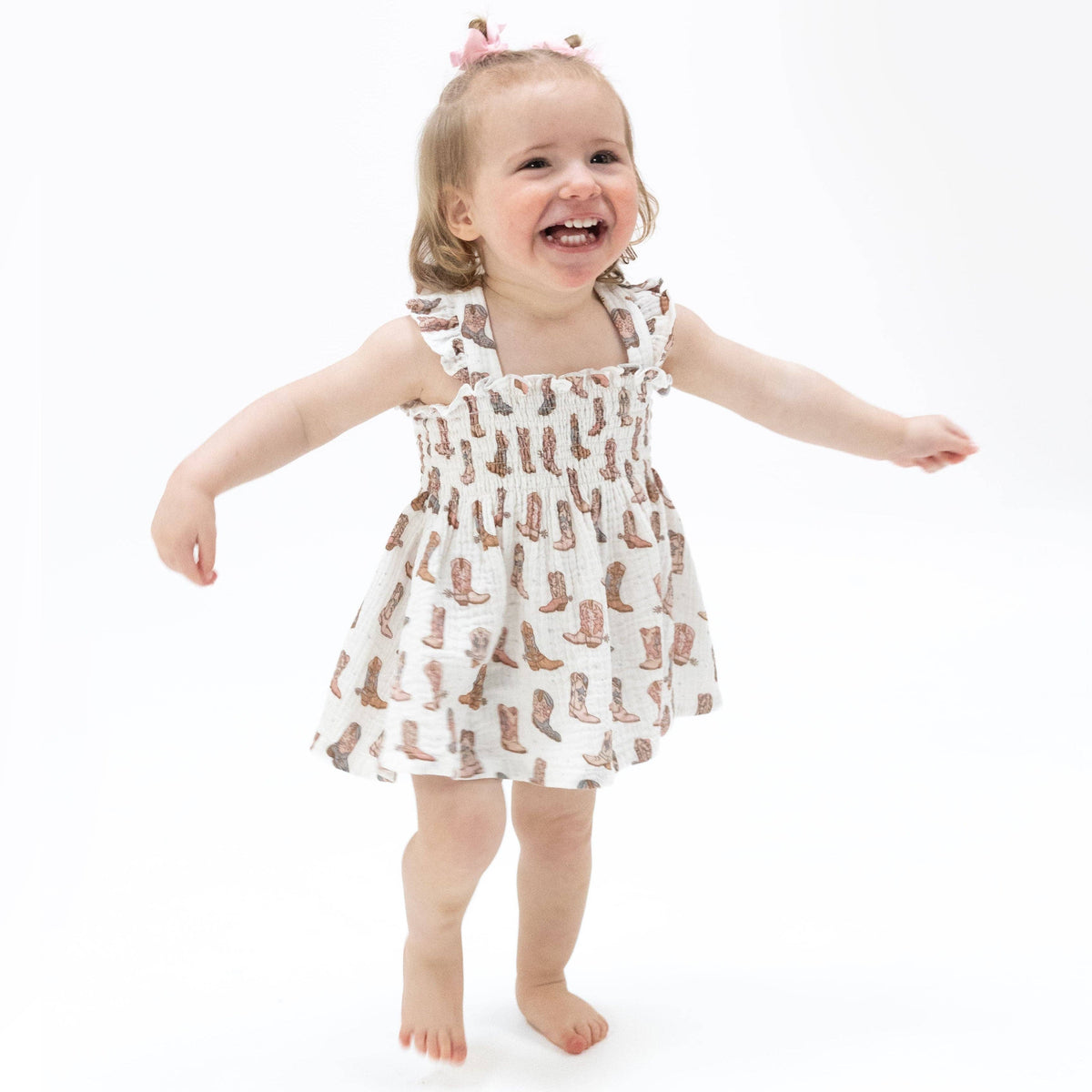 Child wearing a dress with cowboy boot pattern on a white background