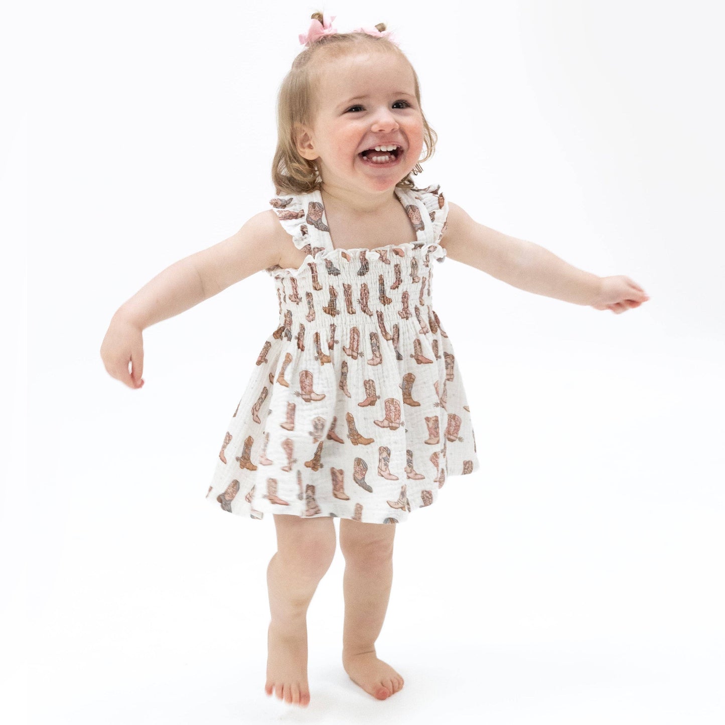Child wearing a dress with cowboy boot pattern on a white background