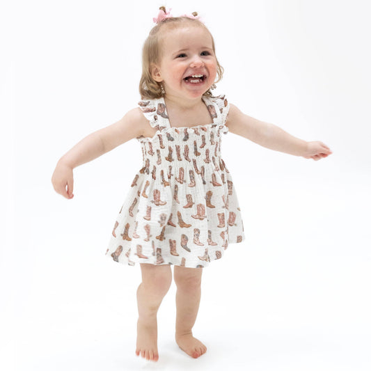 Child wearing a dress with cowboy boot pattern on a white background
