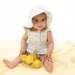 Baby in a lemon-themed outfit holding a basket of lemons on a yellow blanket.