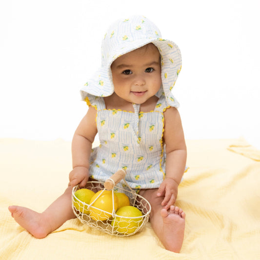Baby in a lemon-themed outfit holding a basket of lemons on a yellow blanket.