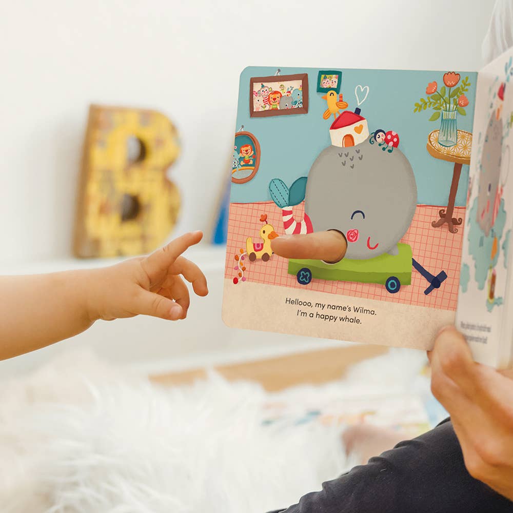 Child's hand pointing at a children's book with a whale illustration on a bed.