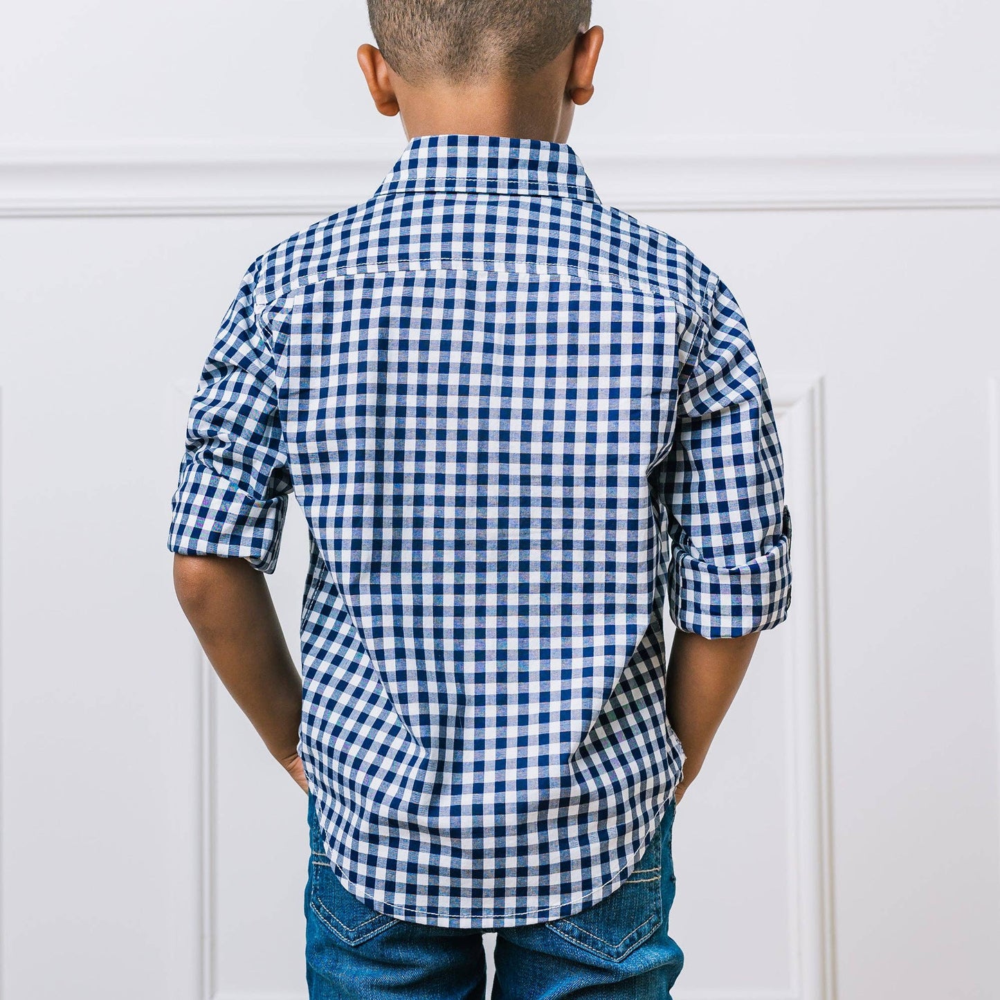 Back of boy wearing a blue and white checkered shirt against a light gray background