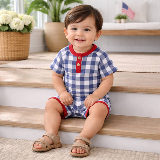 Child wearing a blue and white checkered outfit with red accents, sitting on wooden steps.