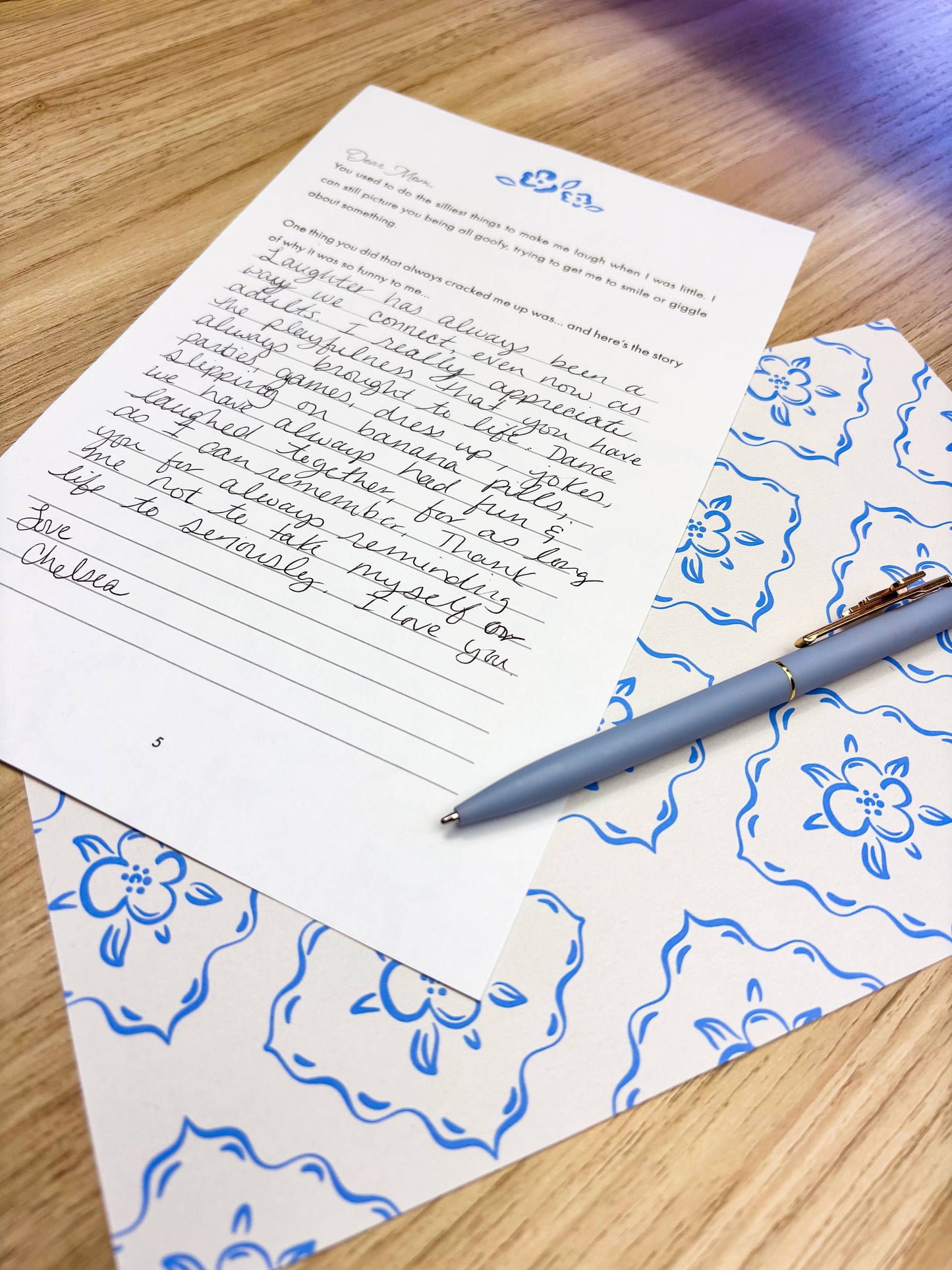 Handwritten letter on floral-patterned paper with a pen on a wooden surface