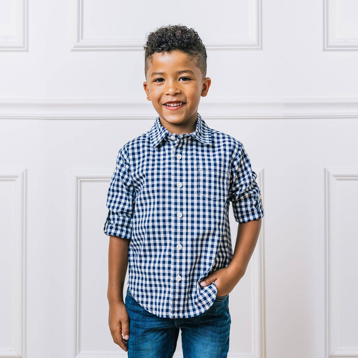 Child wearing a blue and white checkered shirt against a white paneled wall