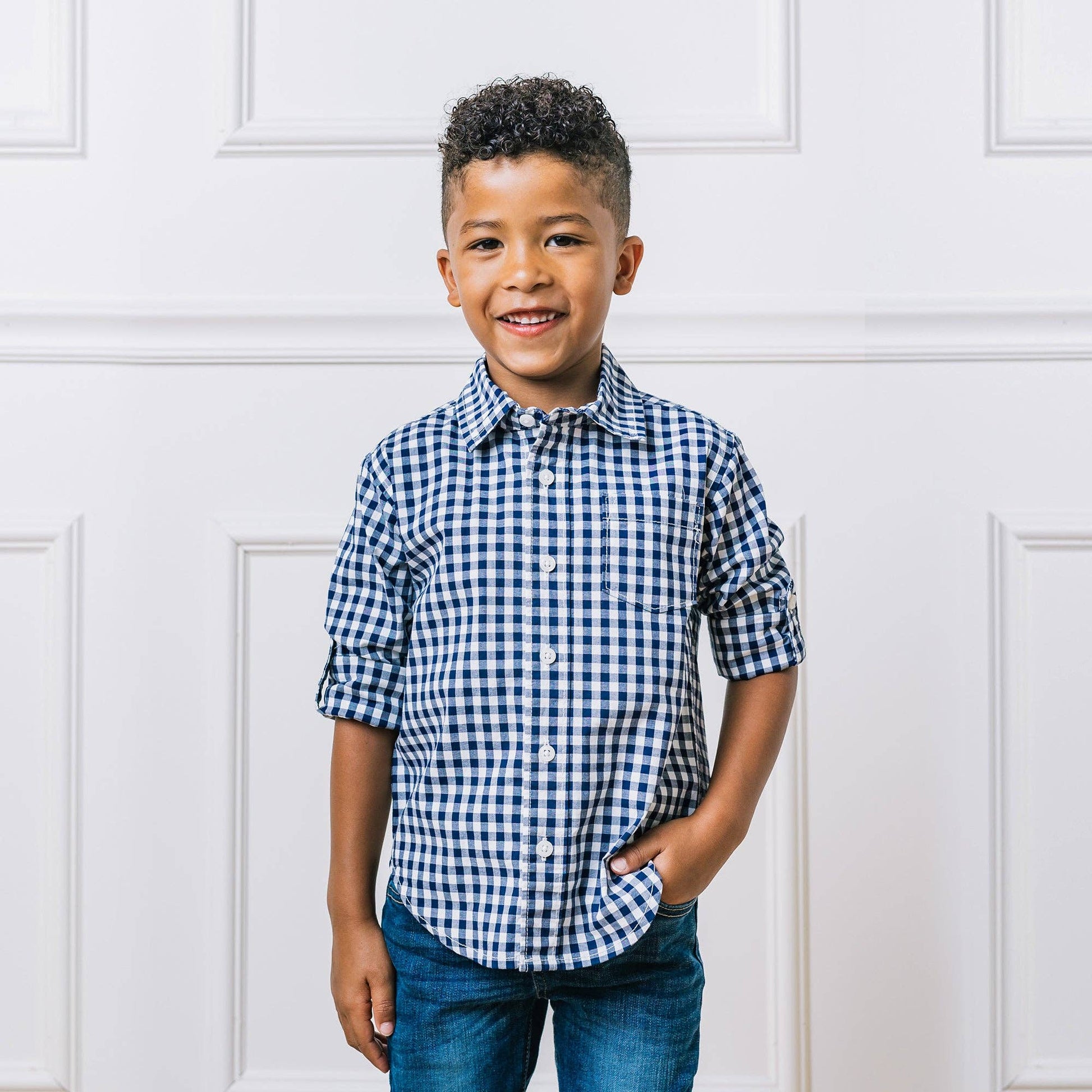 Child wearing a blue and white checkered shirt against a white paneled wall